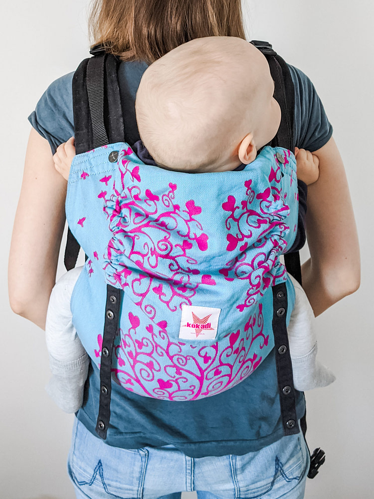 Mom wearing her baby in a full buckle baby carrier on her back Mom wearing her baby in a full buckle baby carrier on her back