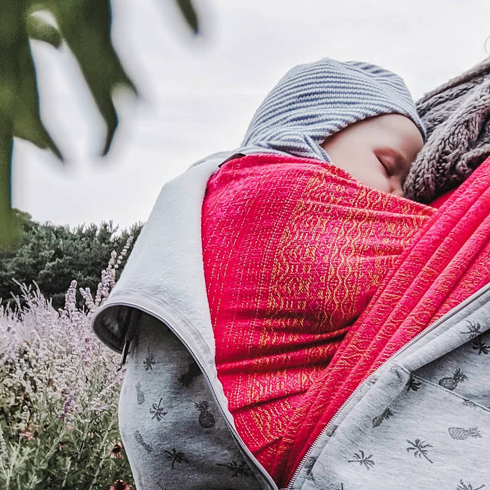 Sleeping baby carried in a pink babywearing wrap. Sleeping baby carried in a pink babywearing wrap.